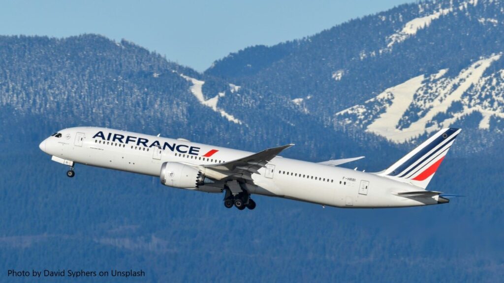 An Air France Boeing 787 Dreamliner aircraft taking off against a backdrop of snow-covered mountains and a clear blue sky.