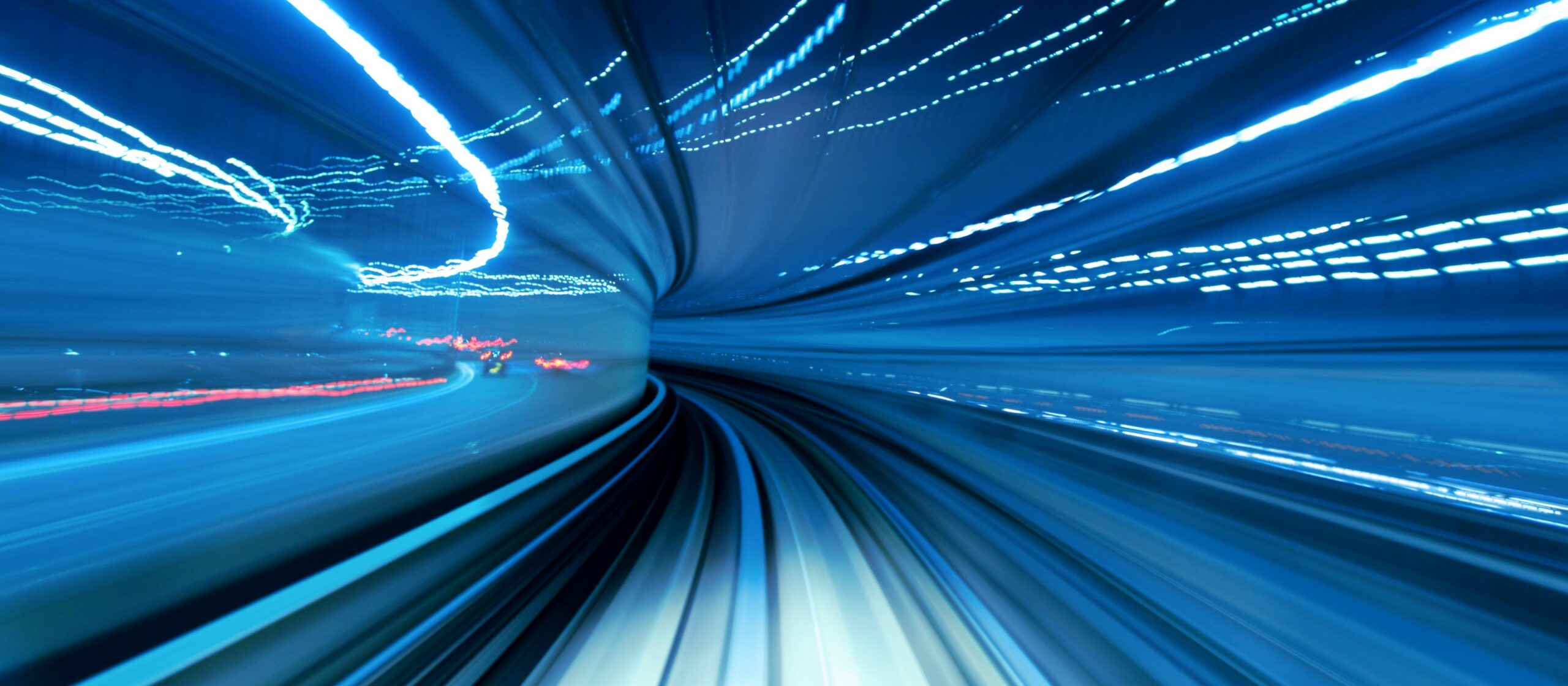 A dazzling, high-speed blur of a train moving through a blue-lit tunnel, creating streaks of light and a sense of intense motion