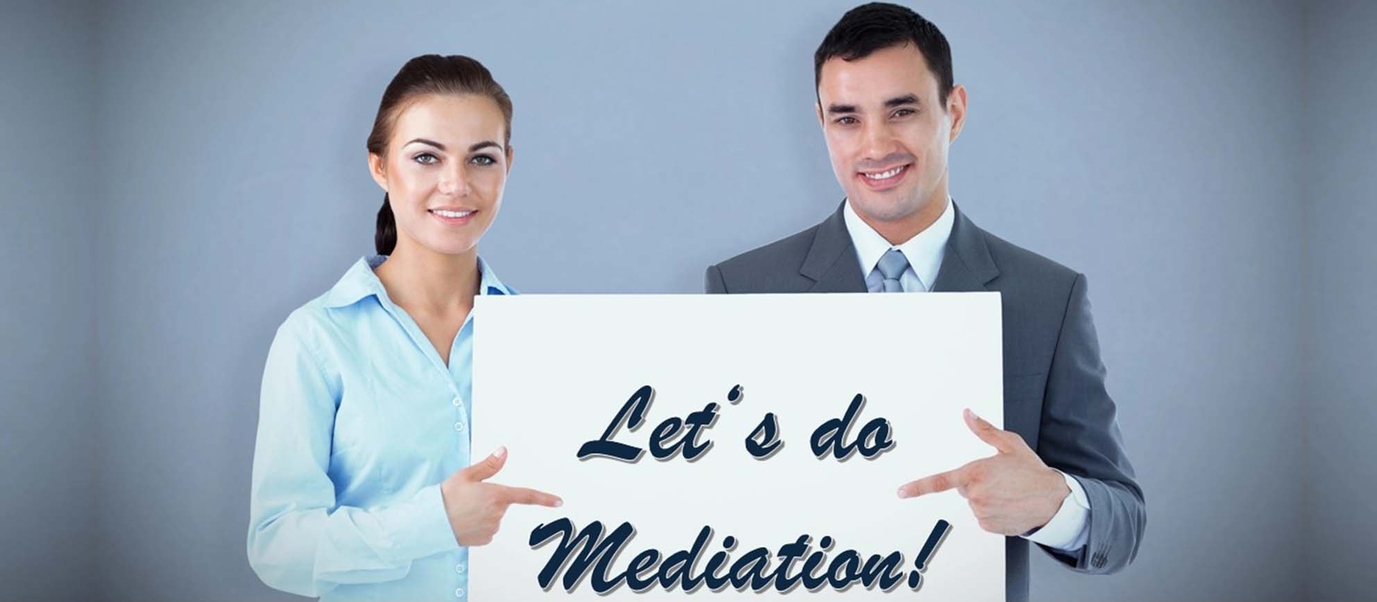 Smiling business people hold a large white sign that reads ‘LET'S DO MEDIATION’.